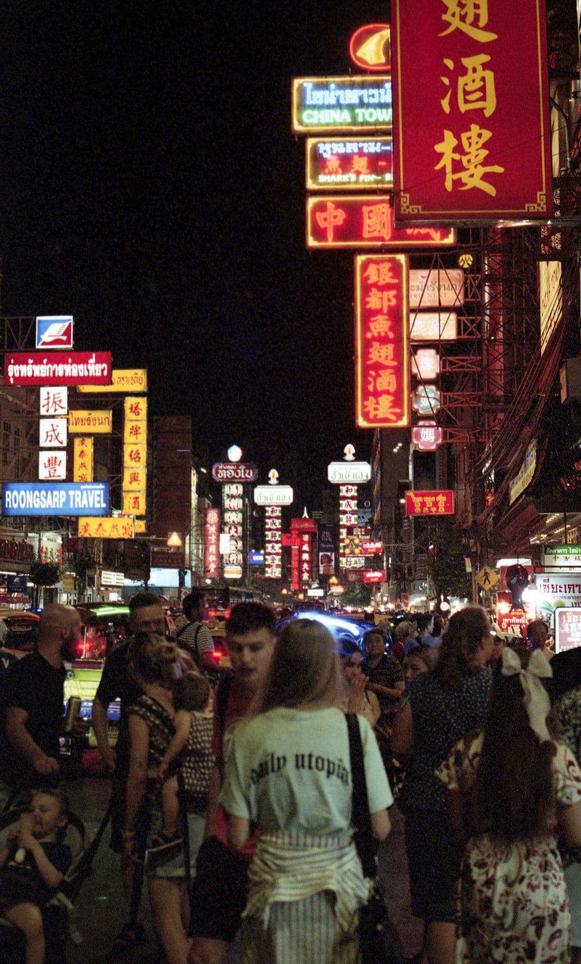 Girl wearing Only Utopia t-shirt in Yaowarat Chinatown Bangkok Thailand by night lit with many neon signs 35mm film photography